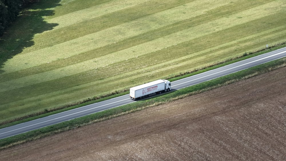White truck driving on a road through green fields